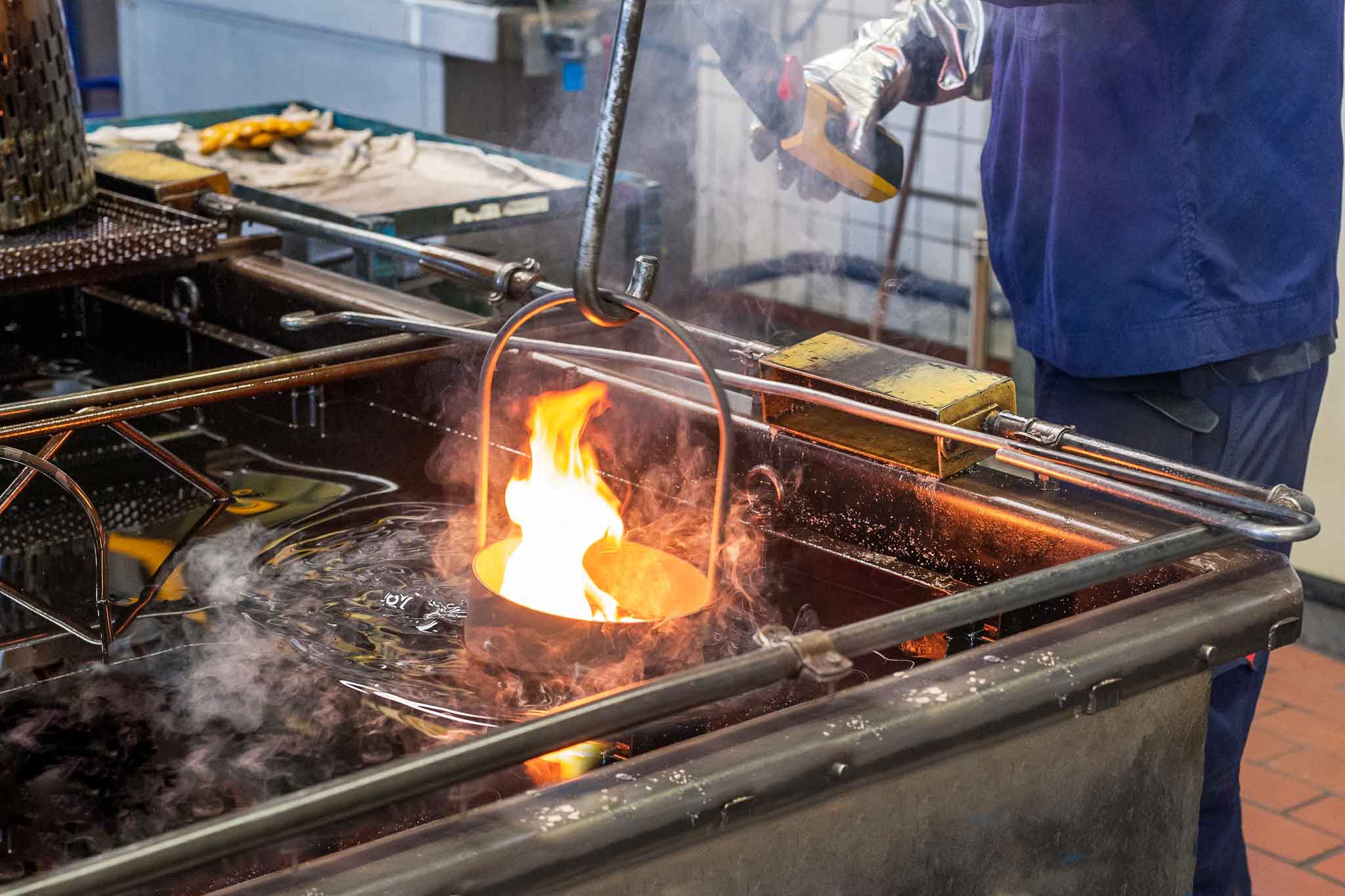 Der Korb mit den Bauteilen wird in eine offene Wanne mit Öl getaucht. Dabei entsteht eine Flamme.