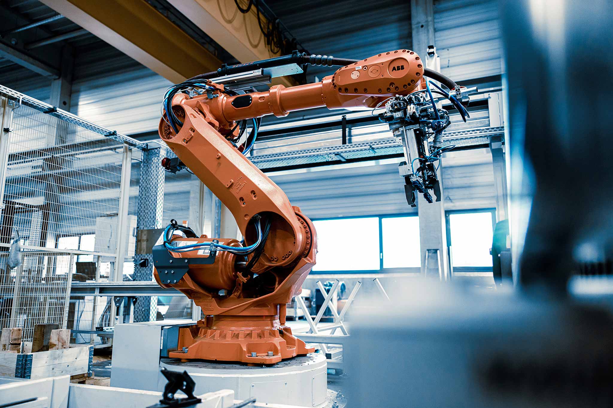 In einer Produktionshalle ist ein oranger Roboter zu sehen, der eine Bearbeitungsmaschine belädt.
