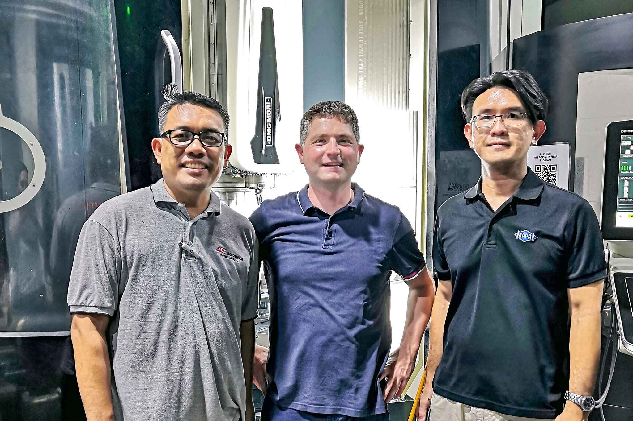 Three employees from SMEA and MAPAL stand in front of a machine.