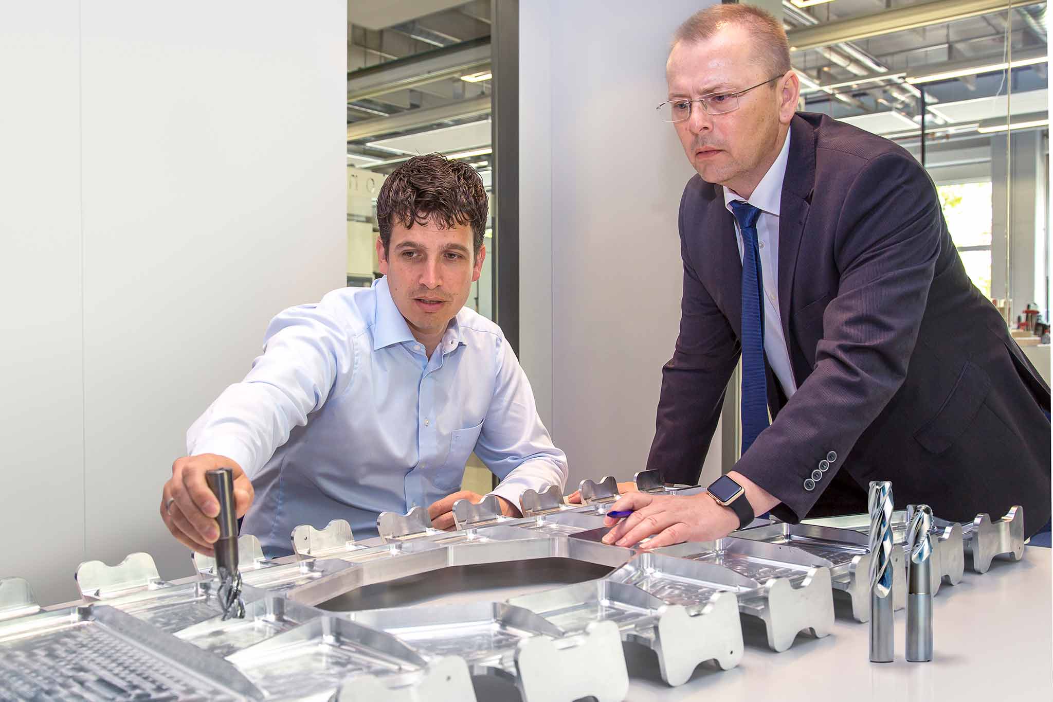 Vor Dietmar Maichel und Axel Fleischer liegt ein großes Strukturbauteil. Daneben stehen Fräser für dessen Bearbeitung.