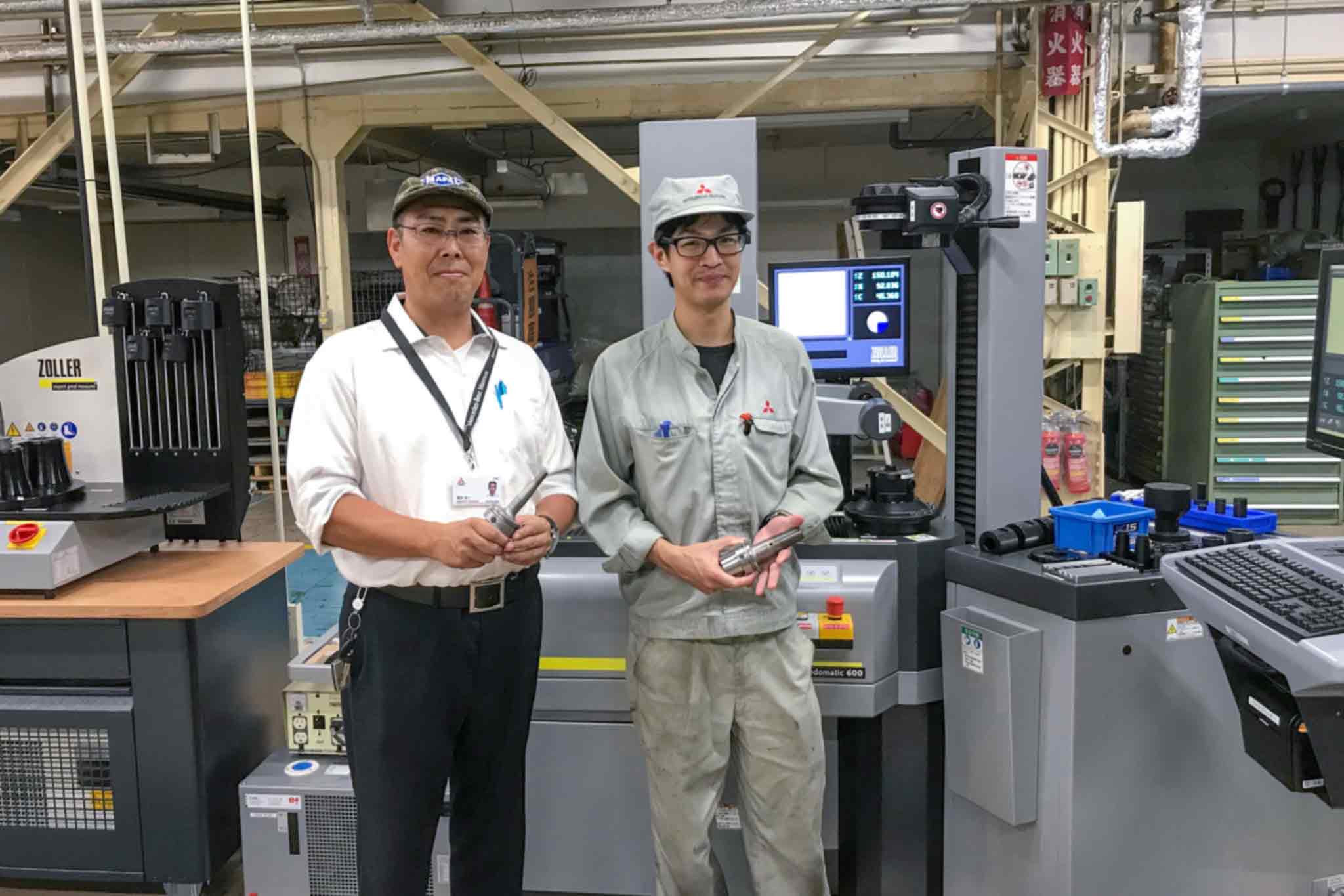 Naoto Katayama und Koichi Fukui stehen in der Fertigung. Beide halten ein Schrumpffutter in den Händen.