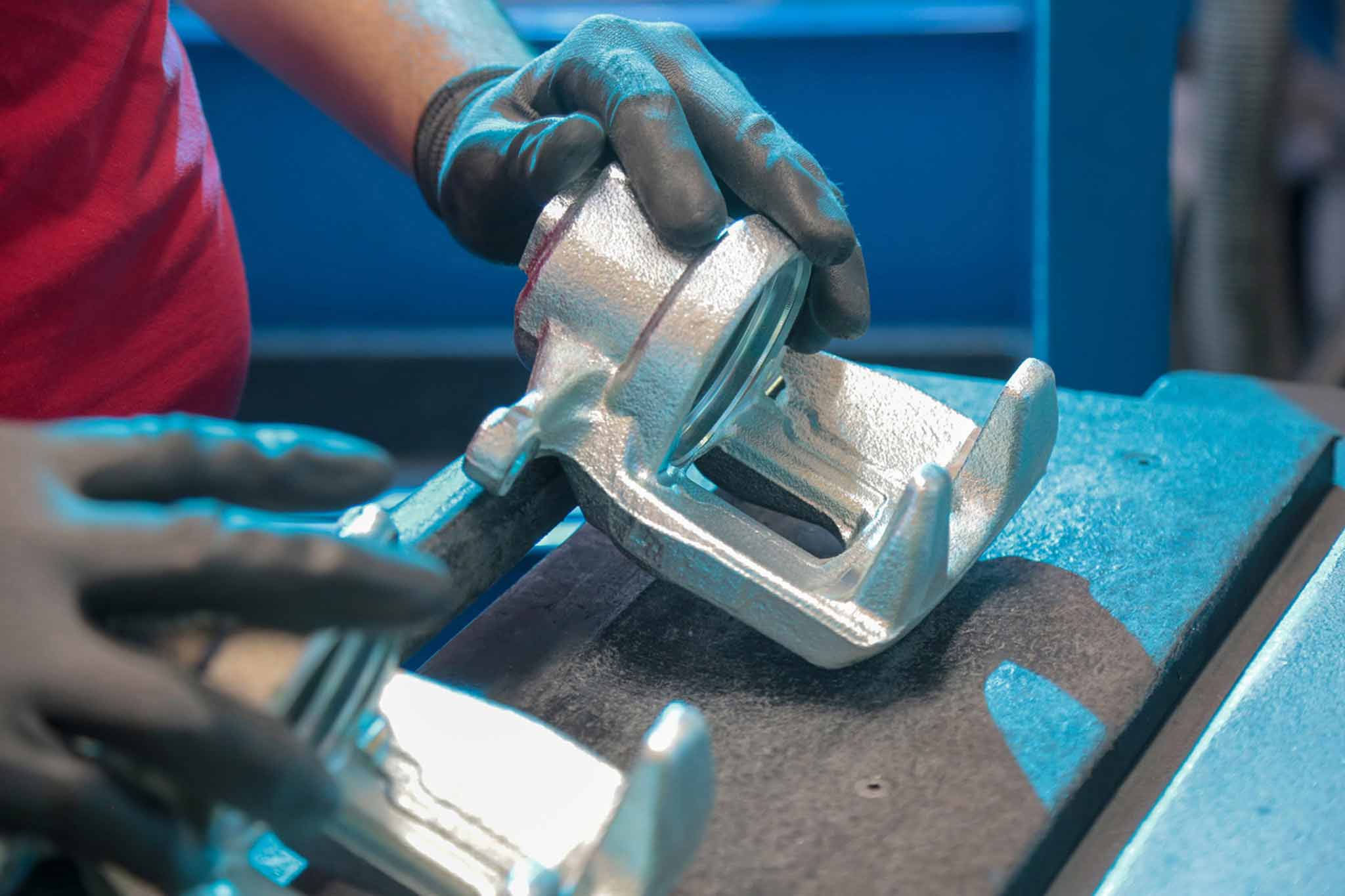 Ein Mitarbeiter von Hitachi Automotive Systems mit Handschuhen nimmt einen Bremssattel aus der Maschine.